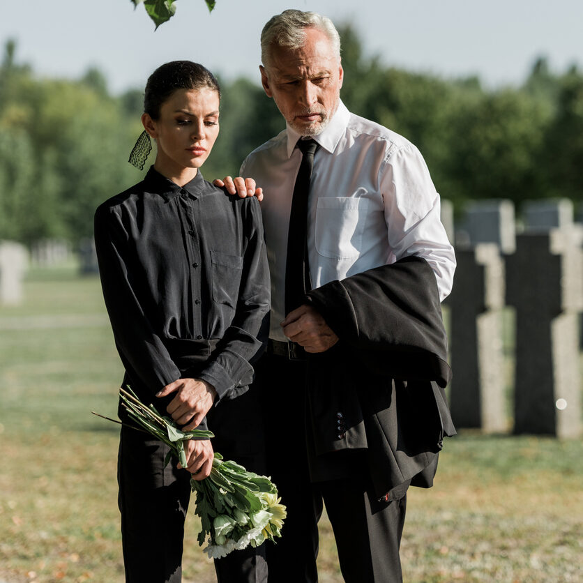 senior man standing with woman holding flowers on funeral