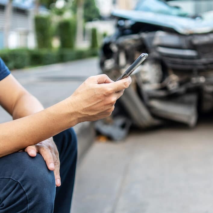 Man calling with phone to his insurance agent after traffic accident with a background of the crashed car, Car insurance an non-life insurance concept.