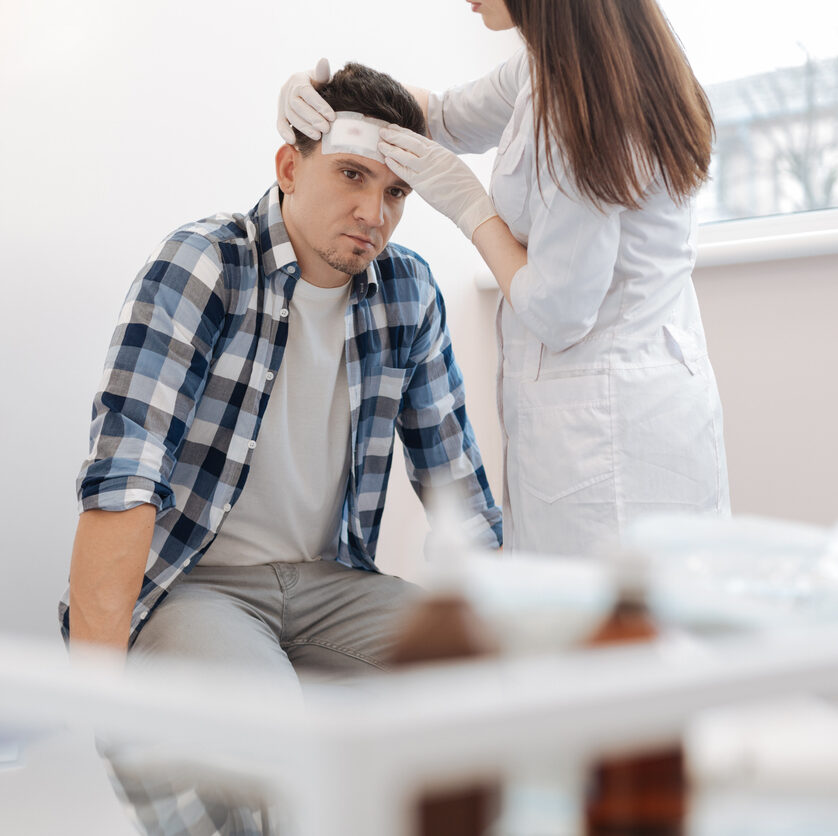man sitting on the medical bed and receiving the first aid while having the forehead wound